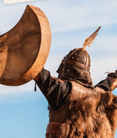 Personne en tenue traditionnelle levant un grand tambour vers le ciel